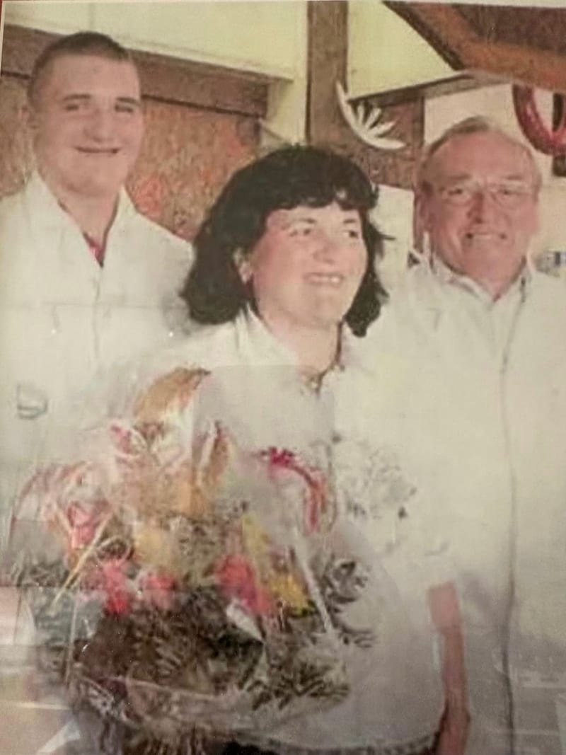 Historische Aufnahme aus der Familiengeschichte: Drei Personen stehen zusammen, im Vordergrund ein großer Blumenstrauß.